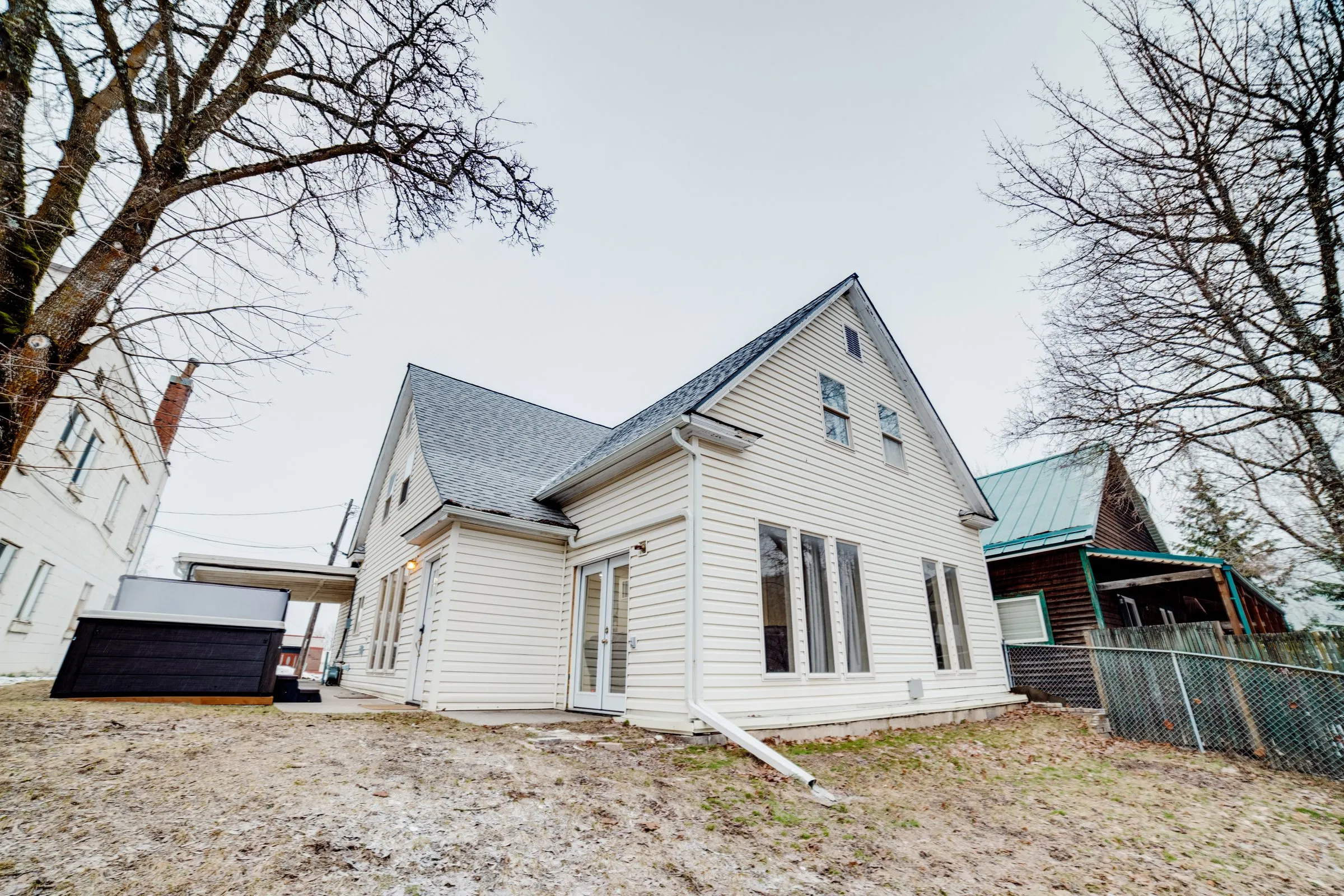 Exterior of the white farmhouse-style home with a large backyard and covered hot tub