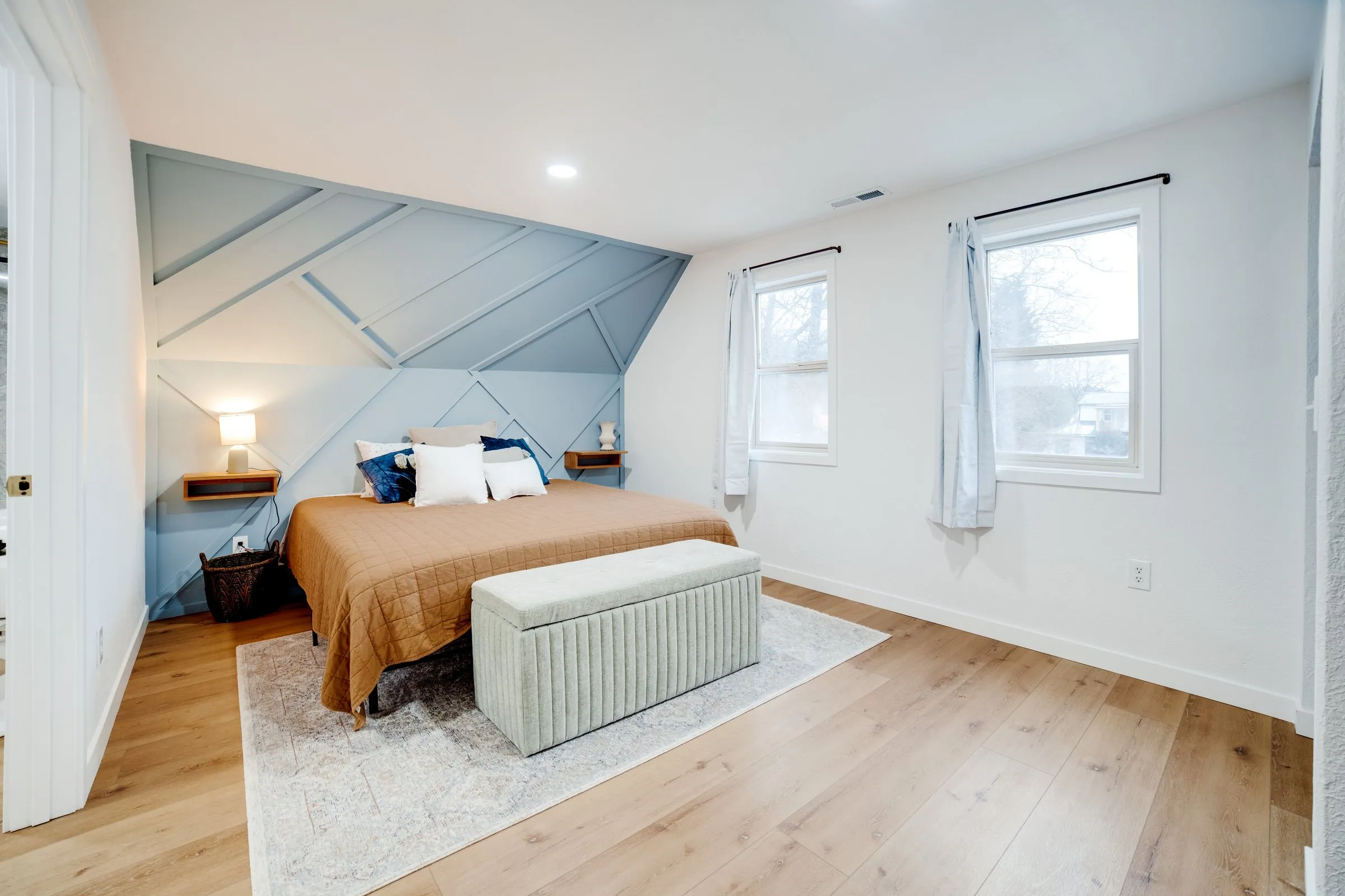 Upstairs bedroom with blue geometric accent wall, rust quilt and upholstered bench
