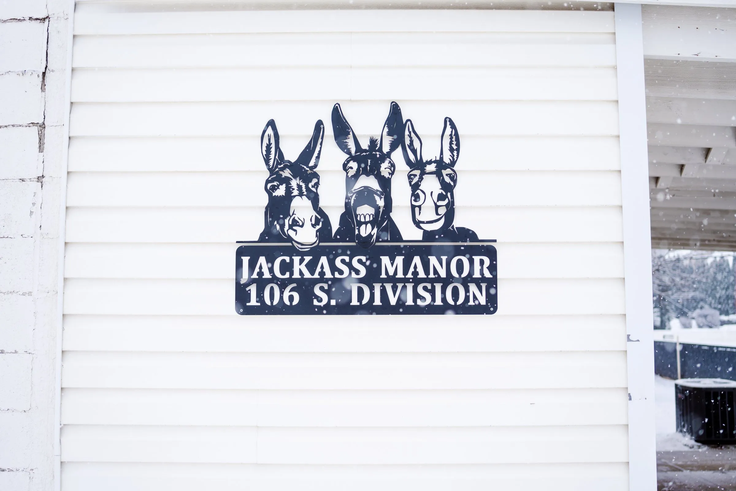 Three-donkey metal sign reading Jackass Manor, 106 S. Division, on the white siding of the Kellogg vacation home