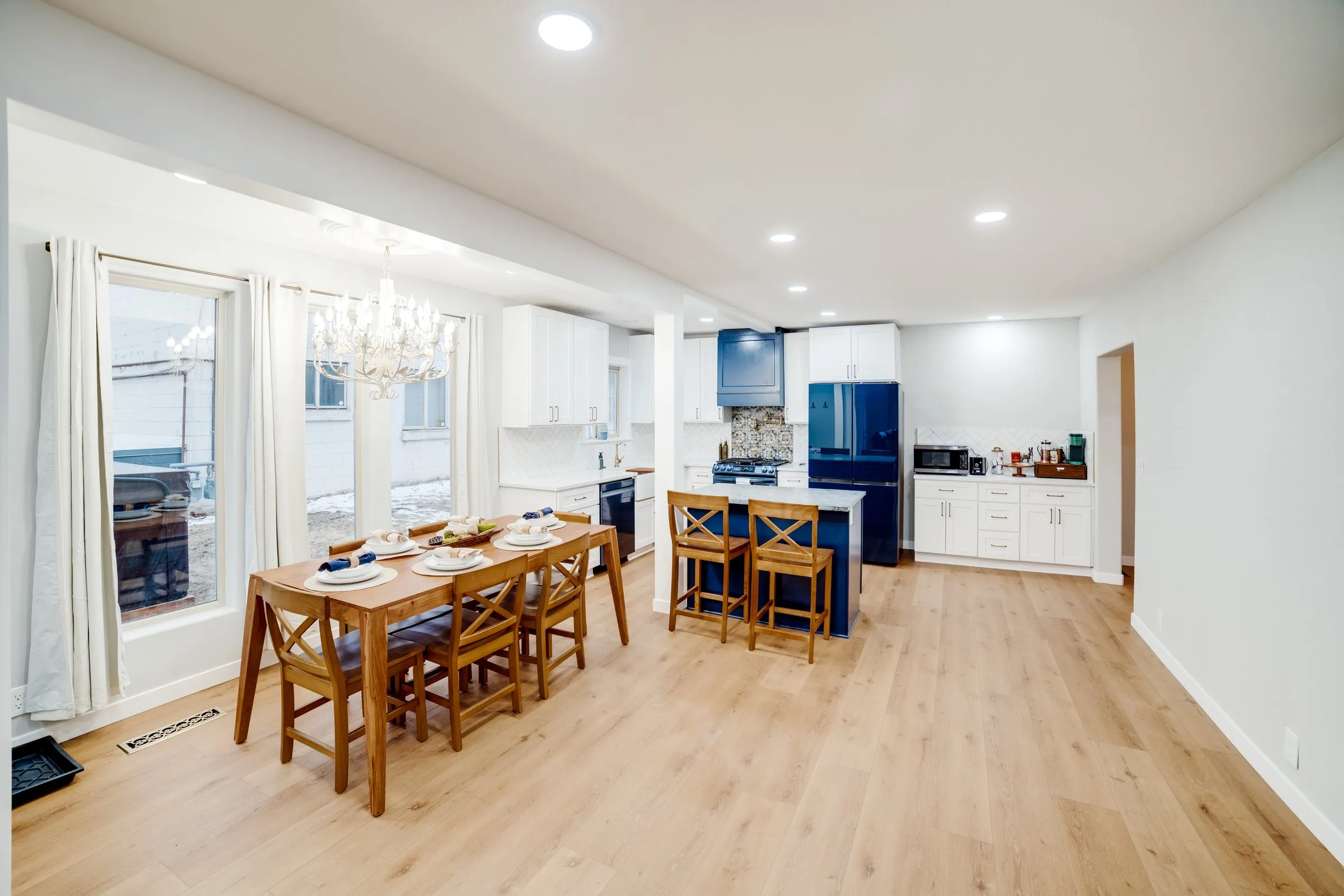 Bright open-concept kitchen and dining room with navy accents, brass hardware and a crystal chandelier