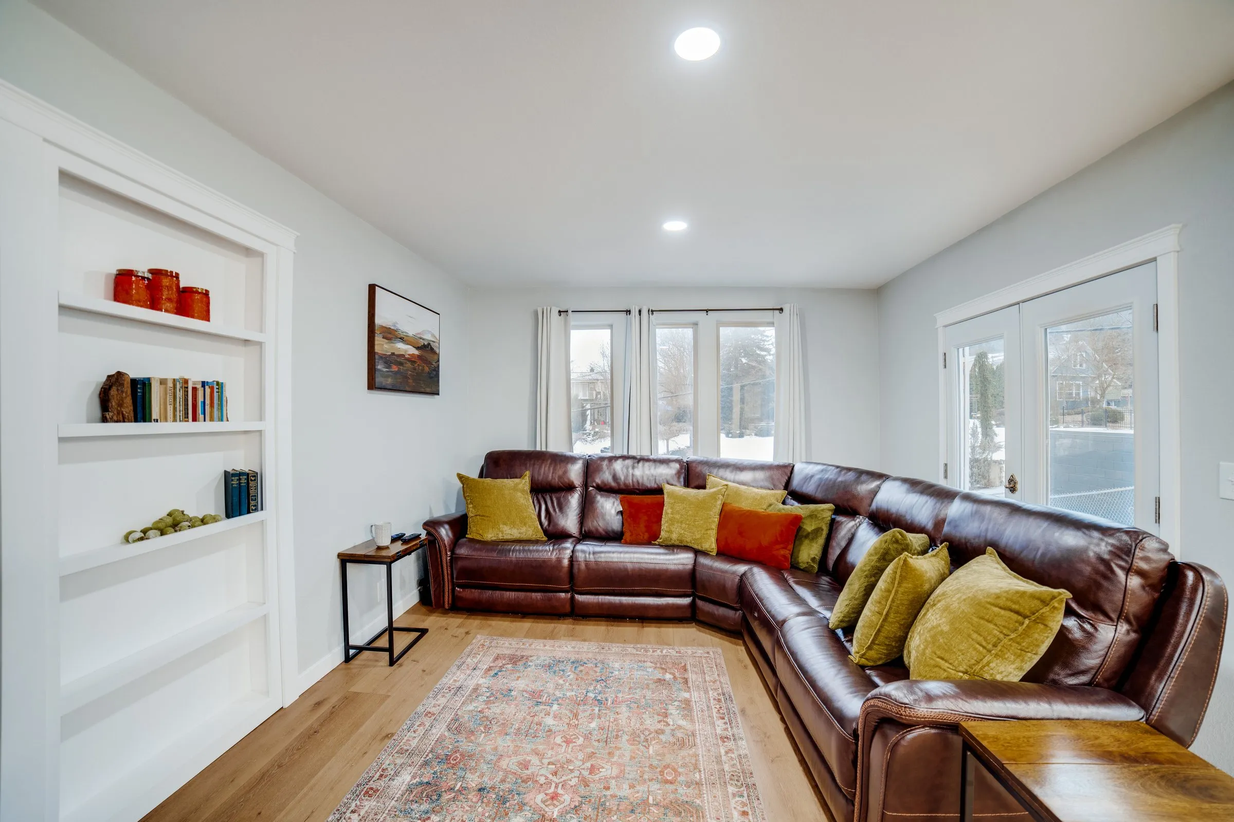 Living room with a reclining leather sectional, mustard pillows, vintage rug and French doors