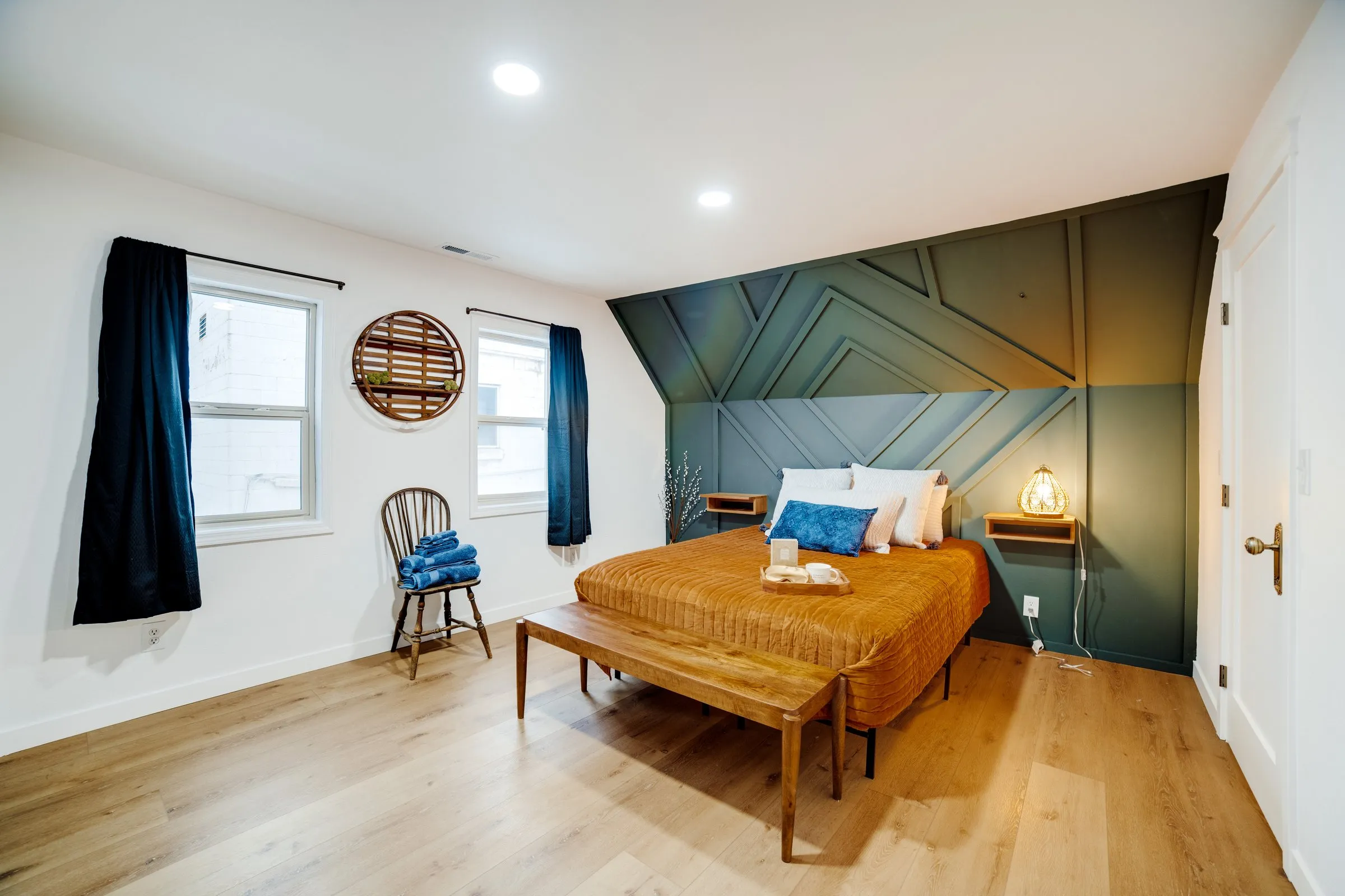 Upstairs bedroom with rust bedding, pine-green geometric accent wall and reading chair